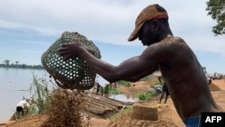 Odilon Salima empties a basket filled with sand, that was collected from the Ubangi river, on the banks of the river in Bangui on November 8, 2023.