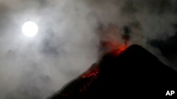 The super blue blood moon sets before dawn as lava cascades down the slopes of Mount Mayon volcano during a mild eruption as seen from Sto. Domingo township, Albay province around 340 kilometers (200 miles) southeast of Manila, Philippines, Feb. 1, 2018.