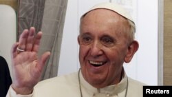 FILE - Pope Francis waves during the media's meeting aboard the papal plane while en route to Rome, Italy, Nov. 30, 2015.