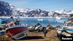 Seorang pria berjalan ke kapal miliknya melewati rongsokan kapal di Kota Tasiilaq, Greenland, 15 Juni 2018.