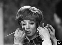 FILE - Make up   and hairsbreadth  artists adhd  the finishing touches to British histrion   Maggie Smith earlier  she faces the camera with Peter Ustinov successful  the drama  'Hot Millions' being filmed astatine  Elstree Studios, England, Jan. 12, 1968.