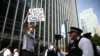 A Just Stop Oil climate activist waves while being filmed by a police officer after activists threw orange paint at the UK headquarters of TotalEnergies in the Canary Wharf district in London on June 27, 2023 to protest against the construction of the Eas