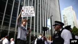 A "Just Stop Oil" climate activist waves while being filmed by a police officer after activists threw orange paint at the U.K. headquarters of Total Energies in London on June 27, 2023 to protest against the construction of the East African Crude Oil Pipeline (EACOP) in Uganda. 