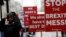 An anti Brexit protester with placards, stand in the rain as they demonstrate outside the Houses of Parliament in London, Tuesday, April 2, 2019. 