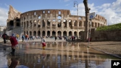 Niños juegan en un charco, junto al Coliseo en Roma, un día después de que fuertes cientos y aguaceros azotaran la capital italiana.