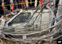 People stand on top of a damaged car at the scene of a missile strike in the southern suburbs of Beirut, Sept. 20, 2024.