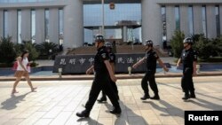 FILE - Policemen patrol as a woman walks past in front of a court, where a trial of suspects of the Kunming railway station attack is taking place, in Kunming, Yunnan province September 12, 2014. Four people accused of participating in an attack at a trai