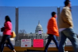 Personas pasan frente a carteles colgados en una valla de seguridad, cerca del Capitolio, en apoyo a la expansión del derecho al voto. Washington DC, domingo 7 de marzo de 2021.