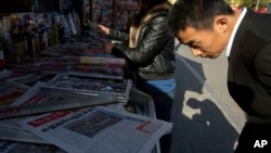 A man looks over near the front page of a Chinese newspaper showing a photo of the typhoon damage in the Philippines and the white characters on blue which reads "U.S. and Europe hype up Chinese aid to Philippines as 'Not Generous'", at a newsstand in Beijing, Nov. 14, 2013. 