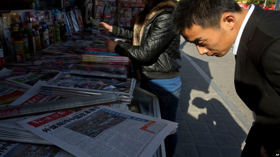 Seorang pria membaca koran China yang dijual di kios di Beijing.
