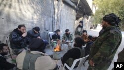 FILE - Rebel fighters of al-Jabha al-Shamiya (Levant Front) warm themselves around a fire near the justice palace in the old city of Aleppo, Syria, Jan. 28, 2016. 