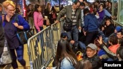 A woman (L) walks past as customers wait in line to buy the newly released iPhone 6 and iPhone 6 Plus, on the first day of sales outside the Apple store at Grand Central Terminal in New York, Sept.19, 2014.