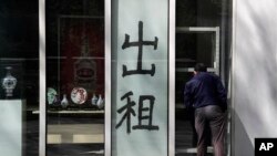 In this April 13, 2020, photo, a man looks at a shuttered shop lot displaying a sign that reads: 'For rent' at a commercial office building in Beijing.