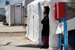 A Syrian displaced woman stands at the entrance of her tent at a refugee camp, in Bar Elias, in eastern Lebanon's Bekaa valley, March 5, 2021.