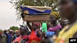 FILE - A woman balances a reed basket holding her child on her head as she stands with fellow villagers waiting to receive food rations at a village in Ayod county, South Sudan, Feb. 6, 2020.