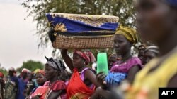 FILE - A woman balances a reed basket holding her child on her head as she stands with fellow villagers waiting to receive food rations at a village in Ayod county, South Sudan, Feb. 6, 2020.