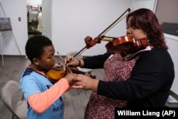 Johnathan Nealy, left, learns how to play the violin as part of an initiative that aims to promote equity in classical music at New Hope Presbyterian Church on Wednesday, Oct. 16, 2024, in Anaheim, California. (AP Photo/William Liang)