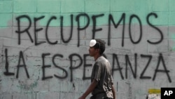 FILE - A man with a misplaced face mask walks past graffiti on a wall that reads in Spanish "Let's get hope back," in Caracas, Venezuela, March 29, 2020.