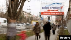 People walk under a poster that reads, "Together with Russia. March 16 - referendum", in the centre of Simferopol, March 12, 2014. 