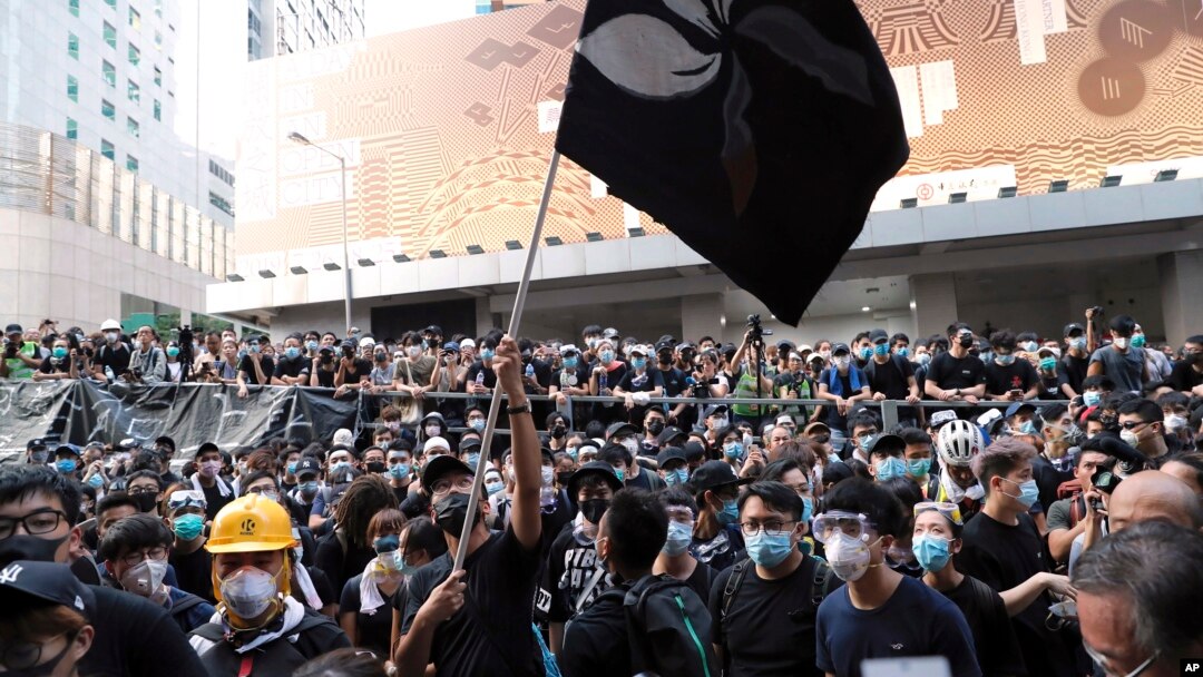 Para pendemo mengibarkan bendera Hong Kong yang dibuat berwarna hitam di depan markas kepolisian di Hong Kong, Jumat, 21 Juni 2019.