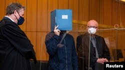 Terdakwa utama menyembunyikan wajahnya saat dia berdiri di antara pengacaranya Udo Vetter dan Wilfried Rath saat mendengar putusan di pengadilan di Muenster, Jerman, dalam kasus pelecehan seksual anak, 6 Juli 2021. (Guido Kirchner/Pool via REUTERS)