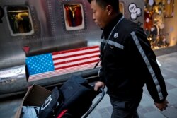 FILE - A delivery man pushes a cart with goods past by a bench with an American flag outside a fashion boutique selling U.S. brand clothing at a mall in Beijing, China, Feb. 1, 2019.