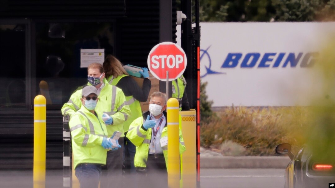 Para petugas mengenakan masker pelindung di pintu masuk ke pabrik produksi Boeing di Everett, Washington, untuk membagikan masker kepada rekan-rekan pekerja lainnya, 21 April 2020, (AP Foto / Elaine Thompson)