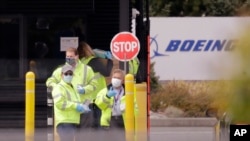 Para pekerja mengenakan baju pelindung berdiri di pintu masuk pabrik pesawat Boeing di Everett, Washington, 21 April 2020. (Foto: AP)