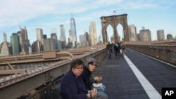 FILE - People eat their breakfast on the Brooklyn Bridge where the Manhattan skyline is seen in the background at the start of a work day, Dec. 3, 2018, in New York. 