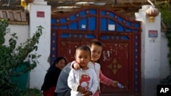 FILE - Uyghur children play while their relatives rest outside their house, decorated with Chinese lanterns and barbed wire at the Unity New Village in Hotan, in western China's Xinjiang region on Sept 20, 2018. 