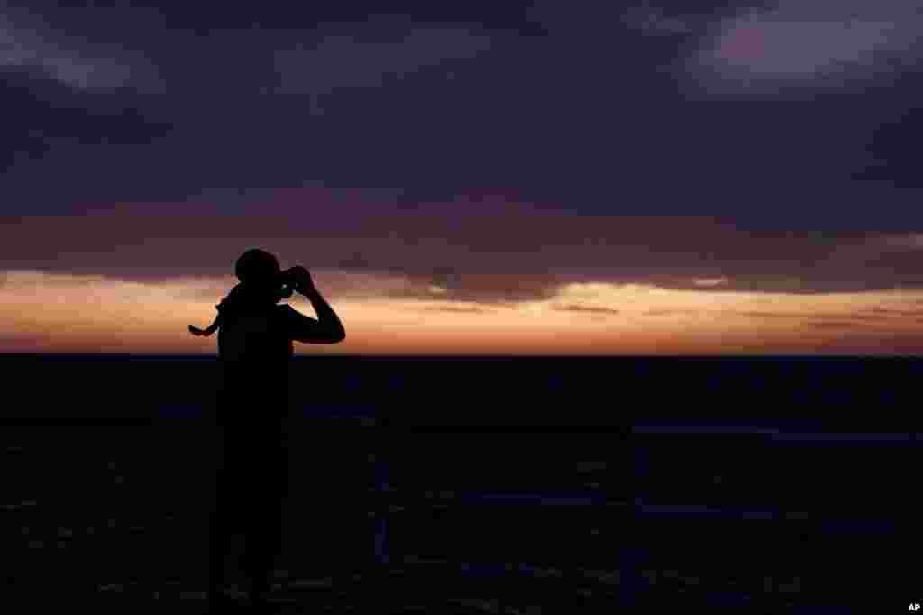 A member of SOS Mediterranee&#39;s Search and Rescue team monitors the horizon at dawn with binoculars for potential boats in distress from aboard the Ocean Viking in international waters north of Libya.