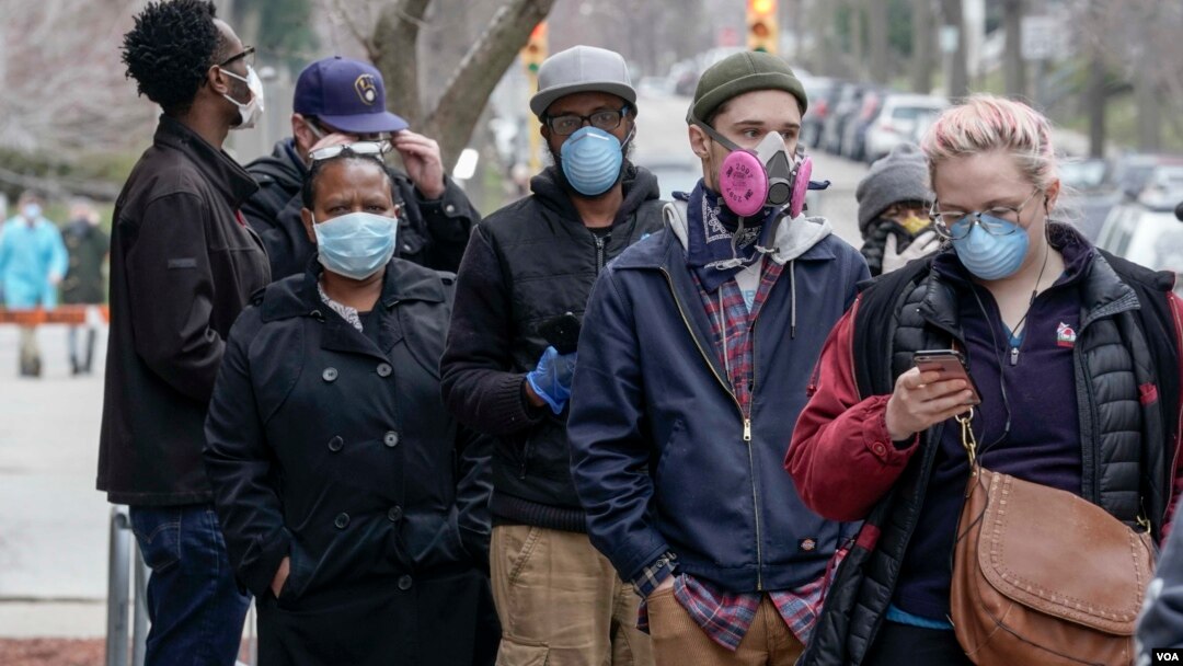 Electores con máscaras faciales hacen fila en la secundaria Riverside de Milwaukee, para votar en la elección primaria de Wisconsin, el 7 de abril de 2020.