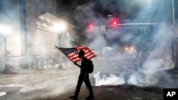 A Black Lives Matter protester carries an American flag as teargas fills the air on July 21, 2020, in Portland, Oregon.