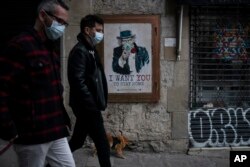 People walk past a poster that reads 'I want you to stay home', by artist TvBoy amid a lockdown in Barcelona, Spain, Tuesday, March 24, 2020. More than 1.5 billion around the world have been told to stay in their homes. (AP Photo/Felipe Dana)