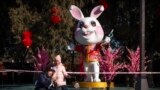 A man and girl pose for a selfie in front a of a statue of a rabbit for the upcoming Lunar New Year at a public park in Beijing, Friday, Jan. 20, 2023. (AP Photo/Mark Schiefelbein)