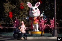 A man and girl pose for a selfie in front a of a statue of a rabbit for the upcoming Lunar New Year at a public park in Beijing, Friday, Jan. 20, 2023. (AP Photo/Mark Schiefelbein)