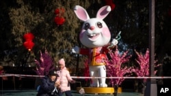 A man and girl pose for a selfie in front a of a statue of a rabbit for the upcoming Lunar New Year at a public park in Beijing, Friday, Jan. 20, 2023. (AP Photo/Mark Schiefelbein)