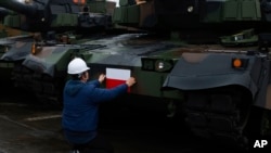 Seorang pekerja memasang bendera Polandia pada tank Black Panther K2 buatan Korea Selatan di pelabuhan Angkatan Laut Polandia, Gdynia, Polandia, 6 Desember 2022. (Foto: Michal Dyjuk/AP Photo)