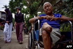 Mantan penderita kusta, Harto, duduk di kursi roda di depan rumahnya di kampung kusta di Tangerang, karena kakinya tidak kuat mengenakan kaki palsu, 18 Januari 2023, (BAY ISMOYO / AFP)