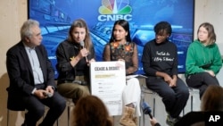 Climate activists sit together with a notice to fossil fuel CEOs, beside Fatih Birol, Head of the International Energy Agency, left, on the sidelines of the World Economic Forum in Davos, Switzerland, Jan. 19, 2023.