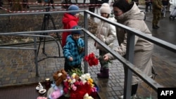 A local resident and children lay flowers at the site where a helicopter crashed near a kindergarten in Brovary, outside the capital Kyiv, Jan. 18, 2023
