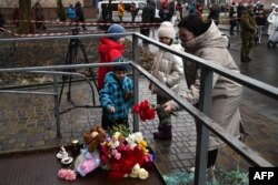 A local resident and children lay flowers at the site where a helicopter crashed near a kindergarten in Brovary, outside the capital Kyiv, Jan. 18, 2023