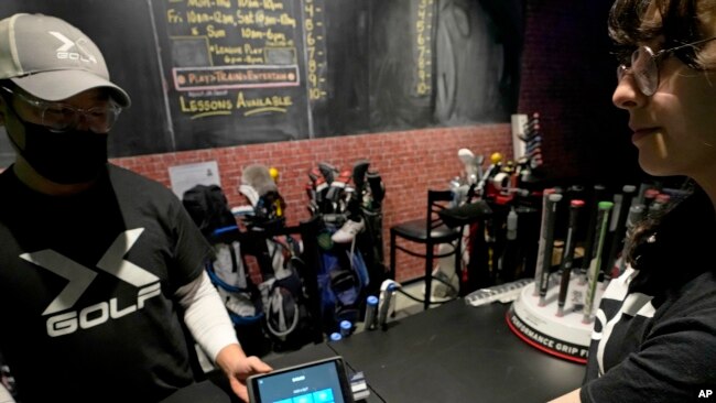 FILE - An employee helps a customer check out at X-Golf indoor golf in Glenview, Ill., Jan. 20, 2023.