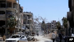 FILE — Syrians walk through destruction in the town of Douma, the site of a suspected chemical weapons attack, near Damascus, Syria, April 16, 2018.
