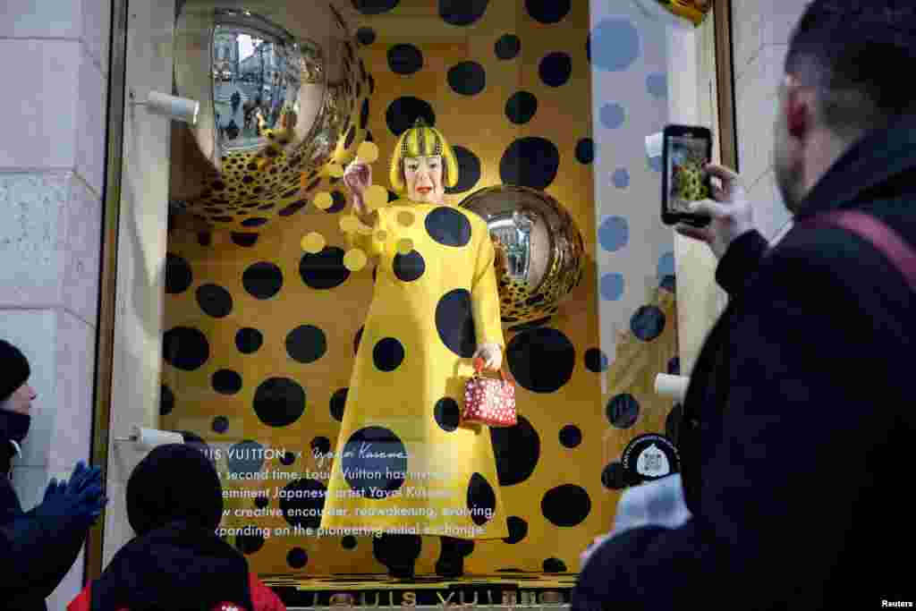 People watch as a lifelike robot of Japanese artist Yayoi Kusama paints spots on the window of the luxury retailer Louis Vuitton store at Place Vendome in Paris, France.