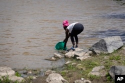 Anne Nduta, 25, collects water to wash her babies' clothes by hand, from the Athi River south of Nairobi, Kenya, Wednesday, Jan. 11, 2023. (AP Photo/Khalil Senosi)