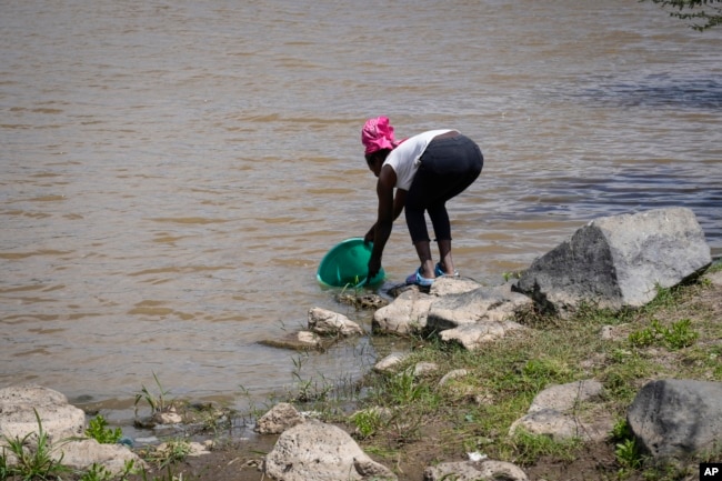 Anne Nduta, 25, collects water to wash her babies' clothes by hand, from the Athi River south of Nairobi, Kenya, Wednesday, Jan. 11, 2023. (AP Photo/Khalil Senosi)