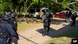 Police in riot gear charge during a training exercise, near a burned passenger van, center, allegedly torched by gangs on Jan. 4, 2023, in Cacahoatan, Mexico, Jan. 18, 2023.