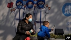 在北京前门街道的一幅抗疫宣传画下，一名幼儿在一名女子的看顾下玩耍。（2021年11月17日）