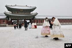 Orang-orang mengenakan pakaian tradisional hanbok menuju Istana Gyeongbokgung saat hujan salju di Seoul, 26 Januari 2023. (Jung Yeon-je / AFP)